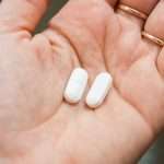 closeup-view-of-a-hand-holding-two-white-pills-in-the-palm-above-a-picture-id1148848404