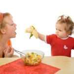 Baby girl feeding her mother with banana – healthy eating concept – isolated