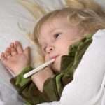 sick child in bed under blanket with thermometer in mouth