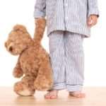 boy in pijama with his teddy bear isolated on white