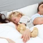 Relaxed little boy sleeping with his parents in their bed at home