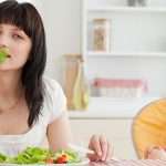 Attractive brunette woman eating a salad next to her baby while