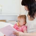 Charming brunette woman showing a book to her baby while sitting