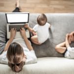 Mother working at home on laptop  multitasking taking care of two children.